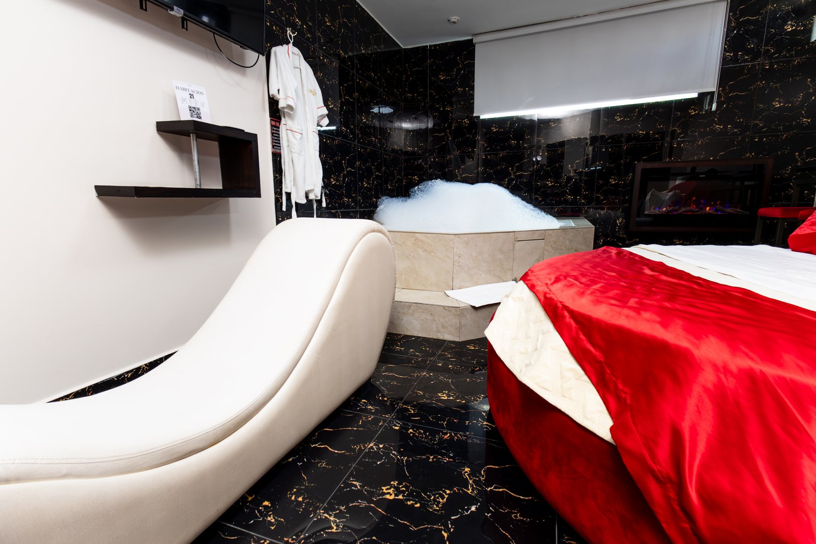 Suite del Hotel Danubio con diván blanco, cama roja y jacuzzi al fondo